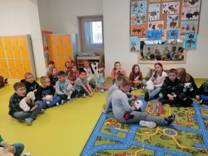 Uczniowie siedzą na podłodze i dywanie trzymając swoje pluszowe misie.