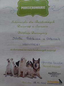 Zdjęcie podziękowań ze schroniska. Na białym tle npisy: "Podziękowanie', "Schronisko dla Bezdomnych zwierzat w Toruniu Dziękuje Darczyńcy Szkoła Podstawowa w Ostaszewie WOLONTARIAT za darowiznę na rzecz bezdomnych zwierząt" U dołu podziękowań zdjęcie siedzących w grupie piesków a obok pieczątka i podpis kierownika Schroniska.