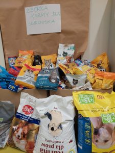 Zdjęcie ułożonych obok siebie różnego rodzaju karmy. Nad nimi kartka z odręcznym napisem :" ZBIÓRKA KARMY DLA SCHRONISKA"