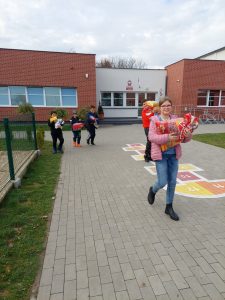 Uczniowie idą szkolnym boiskiem, w ręku trzymaja karmy dla zwierząt.
