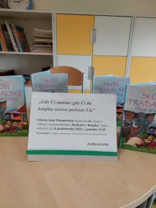 Na stoliku z ustawionymi obok siebie jednakowymi książeczkami ustawiono karteczkę z nadrukiem: "Gdy Ci smutno, gdy Ci źle książka zawsze pocieszy Cię. Szkolne Koło Wolontariatu organizuje dla dzieci z edukacji wczesnoszkolnej "Spotkanie z książką", które odbędzie się 24 października 2022 r. o godzinie 15.45 W programie: czytanie, interpretacja i ilustrowanie wierszy Juliana Tuwima. ZAPRASZAMY".