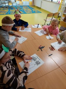 Uczniowie siedzą przy połączonych stolikach, na których kolorują kolorowanki z warzywami.