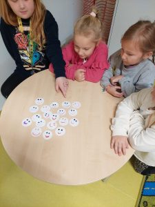 Cztery uczennice siedzą przy okrągłym stoliku, na którym leżą rozłożone białe kułeczka z narysowanymi uśmiechniętymi minkami.