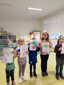 Dzieci stoją w rządku trzymając przed sobą kartki z kolorowymi rysunkami rzepki.