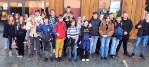 Uczniowie klasy ósmej pozują do zdjęcia grupowego. Dzieci podnoszą dłonie i nimi machają.