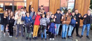 Uczniowie klasy ósmej pozują do zdjęcia grupowego. Dzieci podnoszą dłonie i nimi machają.