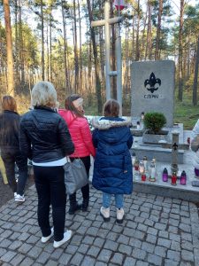 Członkowie szkolnego koła wolontariatu stoją przed pomnikiem Harcerzy na Olku. Przed pomnikiem widać ustawione świeczki.