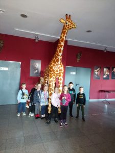 Uczniowie klasy pierwszej pozują do zdjęcia przy dużej żyrafie ustawionej we wnętrzu Baju Pomorskiego.