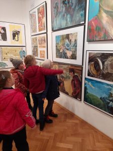 Uczniowie klasy pierwszej oglądająna wystawie zawieszone, kolorowe grafiki.