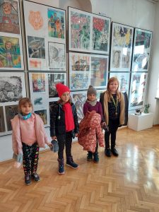 Cztery dziewczynki klasy pierwszej stoją przed grafikami wypełniającymi całą ścianę.