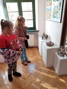 Dwie dziewczynki oglądają stojące na białych postumentach kolorowe figurki.