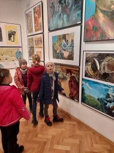 Uczniowie klasy pierwszej oglądająna wystawie zawieszone, kolorowe grafiki.