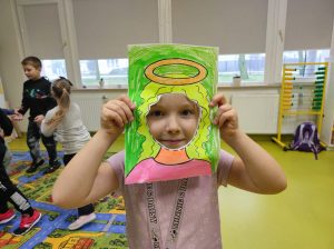 Uczennica przykłada do twarzy wykonaną z papieru ramkę z narysowanymi włosami i aureolą nad nimi.