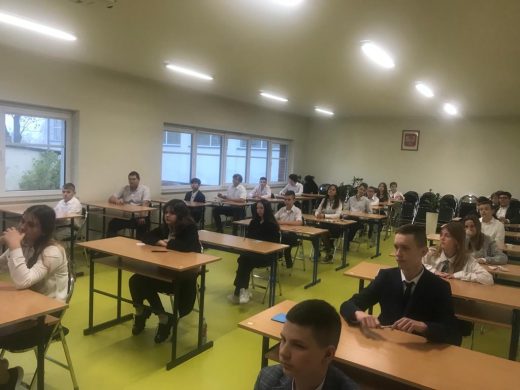 Uczniowie klasy ósmej siedzą przy stolikach na sali teatralnej w oczekiwaniu na egzamin.