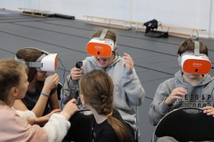 Uczennica oddziału przedszkolnego stoi na tle ustawionej w oknie świątecznej dekoracji. Dziewczynka trzyma przed sobą w dłoniach swoją pracę plastyczną przedstawiającą renifera.