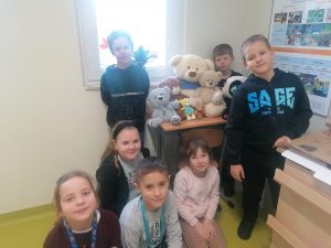 Uczniowie klasy pierwszej pozują do zdjęcia obok stolika, na którym ustawione sa pluszowe misie.