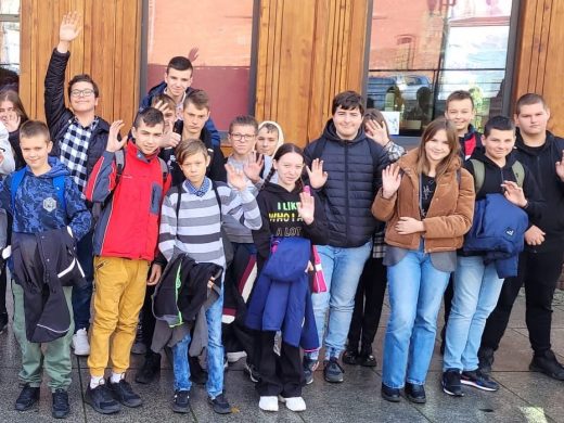 Uczniowie klasy ósmej pozują do zdjęcia grupowego. Dzieci podnoszą dłonie i nimi machają.