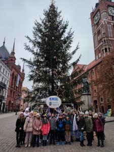 Uczniowie klasy piątej pozują do wspólnego zdjęcia przed choinką ustawioną na starym rynku w Toruniu.