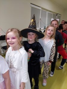 Dziewczynki w kolorowych strojach i z narysowanymi rysunkami na twarzy stoją w jednej kolejce.