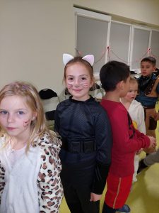 Dziewczynki w kolorowych strojach i z narysowanymi rysunkami na twarzy stoją w jednej kolejce.