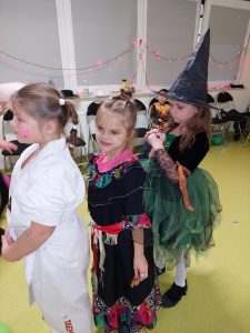 Trzy dziewczynki w kolorowych strojach stoją jedna za drugą w rzędzie.