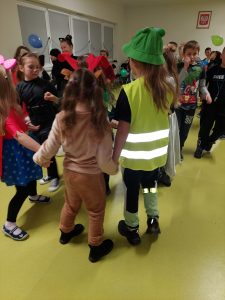 Dzieci w kolorowych przebraniach tańczą w kółeczkach.