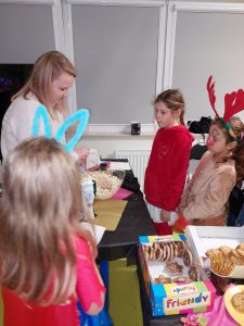 Dwie uczennice stoją w kolejce przy stoliku ze słodkościami.