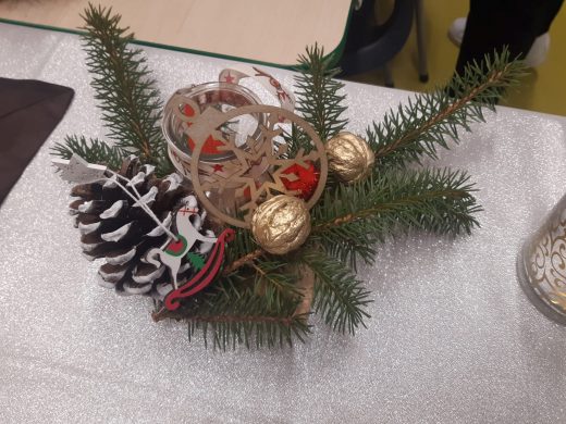 Zdjęcie świątecznego stroika na świeczkę z gałązek sosny ozdobionych drewnianymi elementami i pomalowanymi na złoto orzechami.