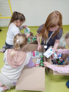 Dziewczynki pakują do dużego pudła kaszki, husteczki i słoiczki przeznaczone dla najmłodszych dzieci.