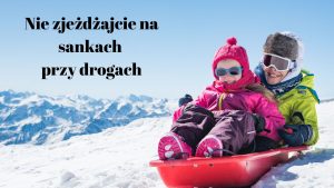 Zdjęcie dwojga dzieci zjeżdżających na sankach z zaśnieżonej górki. Po lewej stronie czarny napis: "Nie zjeżdżajcie na sankach przy drogach".