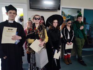 Zwycięzcy i wyróżnieni uczniowie w konkursie na najlepsze przebranie pozują do wspólnego zdjęcia. Uczniowie trzymają w dłoniach dyplomy a zwycięzca papierową torbę z nagrodą.