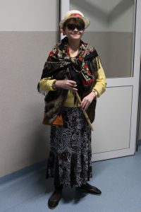Do zdjęcia pozuje uczeń klasy siódmej w stroju babci. Chłopiec w ręku trzyma laskę, na głowie ma kapelusz a na oczach czarne okulary przeciwsłoneczne. Uczeń ubrany jest w długą spódnicę a na ramionach ma zawiązaną chustę w kwiaty.