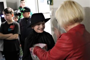 Uczeń klasy czwartej dostaje nagrodę od Pani Dyrektor za najlepszy taniec. Chłopiec szeroko się uśmiecha. W tle widać stojących innych uczniów.