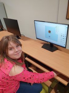 Uczennica siedzi przy komputerze. Głowę odwraca w stronę zdjęcia.