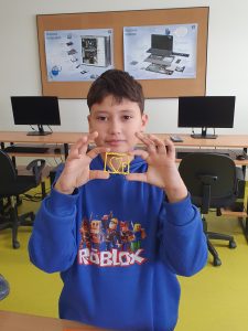 Uczeń pozuje do zdjęcia trzymając przed sobą swoja pracę wykonaną długopisem 3D. Uczeń w prostokątnej żółtej ramce umieścił serduszko i literę F.