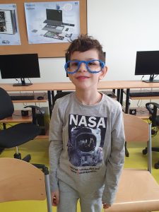 Uczeń pozuje do zdjęcia. Na twarzy ma założone wykonane przez siebie niebieskie okulary.