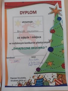 Zdjęcie dyplomu otrzymanego przez Kacpra Stalmierskiego za zajęcie I miejsca w rodzinnym konkursie plastycznym "ŚWIĄTECZNE DRZEWKO". Dyplom ozdobiony grafiką udekorowanej choinki i ułożonymi pod nią prezentami.
