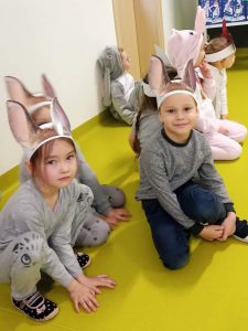 Część uczniów oddziału przedszkolnego podczas występu z okazji dnia babci i dziadka. Dzieci kucają na podłodze. Na głowie mają założone opaski z długimi uszami.