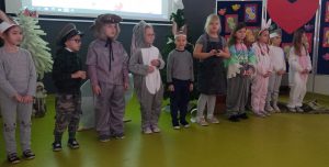 Uczniowie oddziału przedszkolnego podczas wystąpienia z okazji dnia babci i dziadka. Dzieci stoją w jednym rzędzie. Ubrane są w stroje postaci, które odgrywały w przedstawieniu.