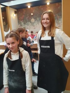 Dwie uczennice klasy piątej pozują do zdjęcia ubrane w czarne fartuchy z białym napisem azzurro.