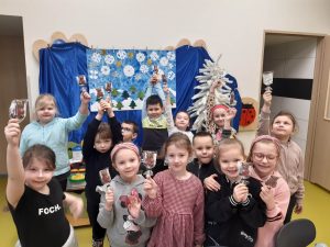 Uczniowie oddziału przedszkolnego pozują do grupowego zdjęcia. Dzieci trzymają w wyciągniętych dłoniach czekoladowe lizaki w kształcie misiów z serduszkami.