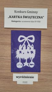 Praca plastyczna nagrodzona w konkursie "Kartka Świąteczna". Nad nagrodzona kartką prostokątna karteczka z nadrukiem :"Konkurs Gminny "KARTKA ŚWIĄTECZNA" Kategoria: uczniowie klas IV-VIII". Pod nagrodzona kartka karteczka z nadrukiem "wyróżnienie" i jeszcze jedna mniejsza z nadrukiem "Emil Lewalski SP Ostaszewo". Kartka przedstawia biały świąteczny stroi na granatowym tle.