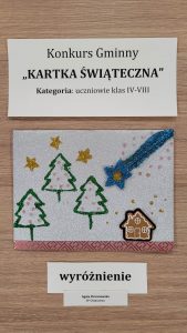 Praca plastyczna nagrodzona w konkursie "Kartka Świąteczna". Nad nagrodzona kartką prostokątna karteczka z nadrukiem :"Konkurs Gminny "KARTKA ŚWIĄTECZNA" Kategoria: uczniowie klas IV-VIII". Pod nagrodzona kartka karteczka z nadrukiem "wyróżnienie" i jeszcze jedna mniejsza z nadrukiem "Agata Chrzanowska SP Ostaszewo". Kartka przedstawia trzy choinki oraz mały piernikowy domek stojący obok nich. Z góry narysowana jest niebieska spadająca gwiazda. Wszystko umieszczone na białym tle i ozdobione złotymi gwiazdkami.