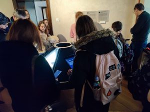 Uczniowie klasy piątej podczas oglądania wystawy w muzeum. Dzieci stoją rozproszone po sali.