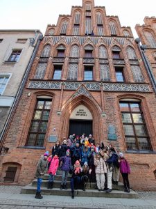 Uczniowie klasy piątej pozują do grupowego zdjęcia przed "Domem Mikołaja Kopernika" w Toruniu.