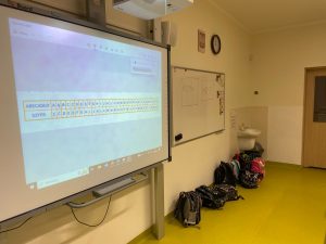 Zdjęcie tablicy interaktywnej na której wyświetlony jest w jednym rzędzie alfabet a pod nimi szyfr - alfabet z przestawioną kolejnością liter.