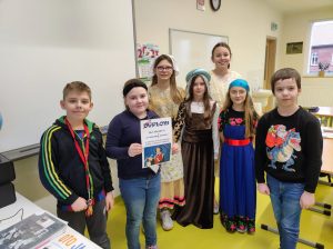 Troje uczniów klasy trzeciej wraz z czteroma dziewczynkami z klasy piątej pozują do wspólnego zdjęcia. Uczennice klasy piątej ubrane są w stroje z epoki Mikołaja Kopernika. Jedna z uczennicy klasy trzeciej trzyma w dłoniach otrzymany dyplom za zajęcie pierwszego miejsca w konkursie wiedzy o Koperniku.