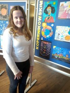 Wyróżniona w konkursie uczennica Roksana Pawlak pozuje do zdjęcia na tle galerii stworzonej z nagrodzonych prac plastycznych.