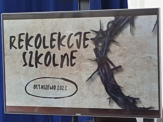 Zdjęcie wyświetlanego na ekranie telewizora slajdu z napisem "REKOLEKCJE SZKOLNE" "OSTASZEWO2023". Obok napisów widoczny jest fragment korony cierniowej. Całość utrzymana w tonacji beżów i szarości.