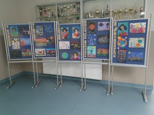 Zdjęcie galerii prac wyróżnionych i nagrodzonych w konkursie. Na pięciu tablicach ustawionych obok siebie umieszczono kolejno napisy tworzące hasło konkursu: "MIESZKAM W CIEKAWYM MIEJSCU PODĄŻAM SZLAKIEM KOPERNIKOWSKIM".